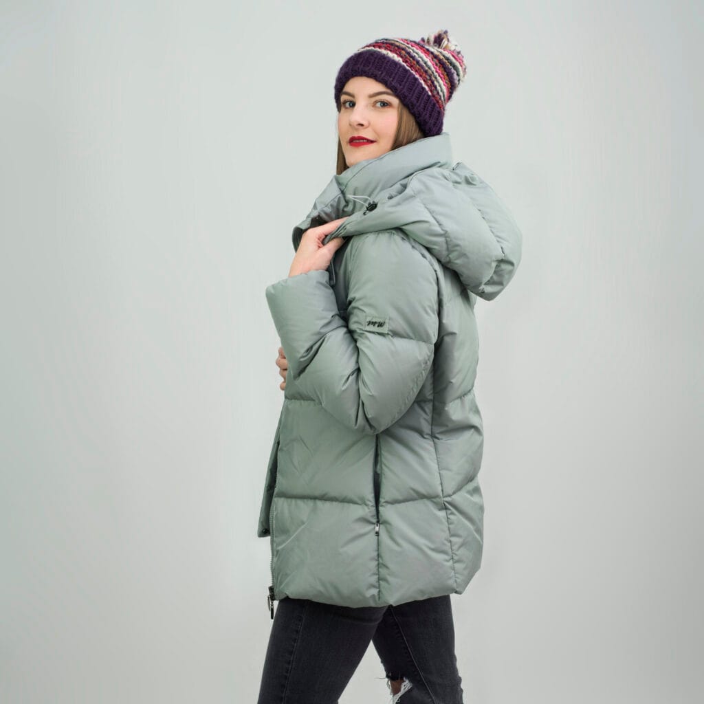 Polskie kurtki puchowe – kobieta w zielonoszarej kurtce z kapturem i kolorowej czapce